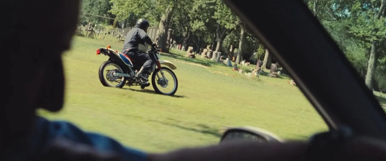 The Place Beyond The Pines (2012) movie still: medium — A sunny cemetery features headstones scattered across a wide grassy expanse with mature…