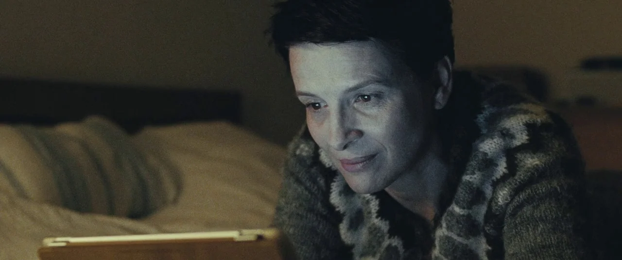 Clouds of Sils Maria (2014) movie still: closeup — A person lies in a darkened room with a blurred bed visible in the background. The individual…
