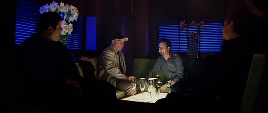 25th Hour (2002) movie still: wide — A dark lounge interior features blue-lit window blinds and low upholstered seating. Four men occupy the space,…