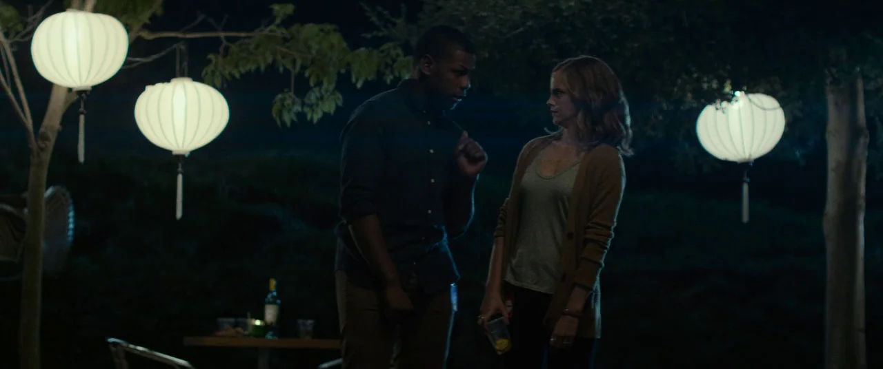 The Circle (2017) movie still: medium — A night setting features several round white paper lanterns suspended from tree branches. A man and woman…