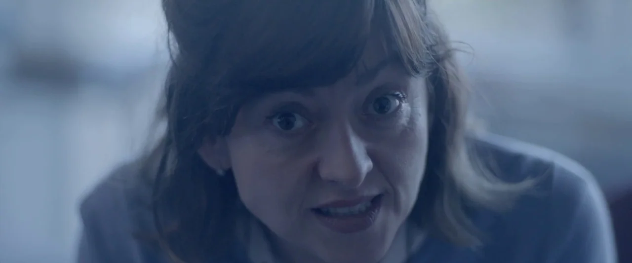 Prevenge (2016) movie still: closeup — A woman's face is positioned centrally against a blurred interior background. She looks directly upward into…