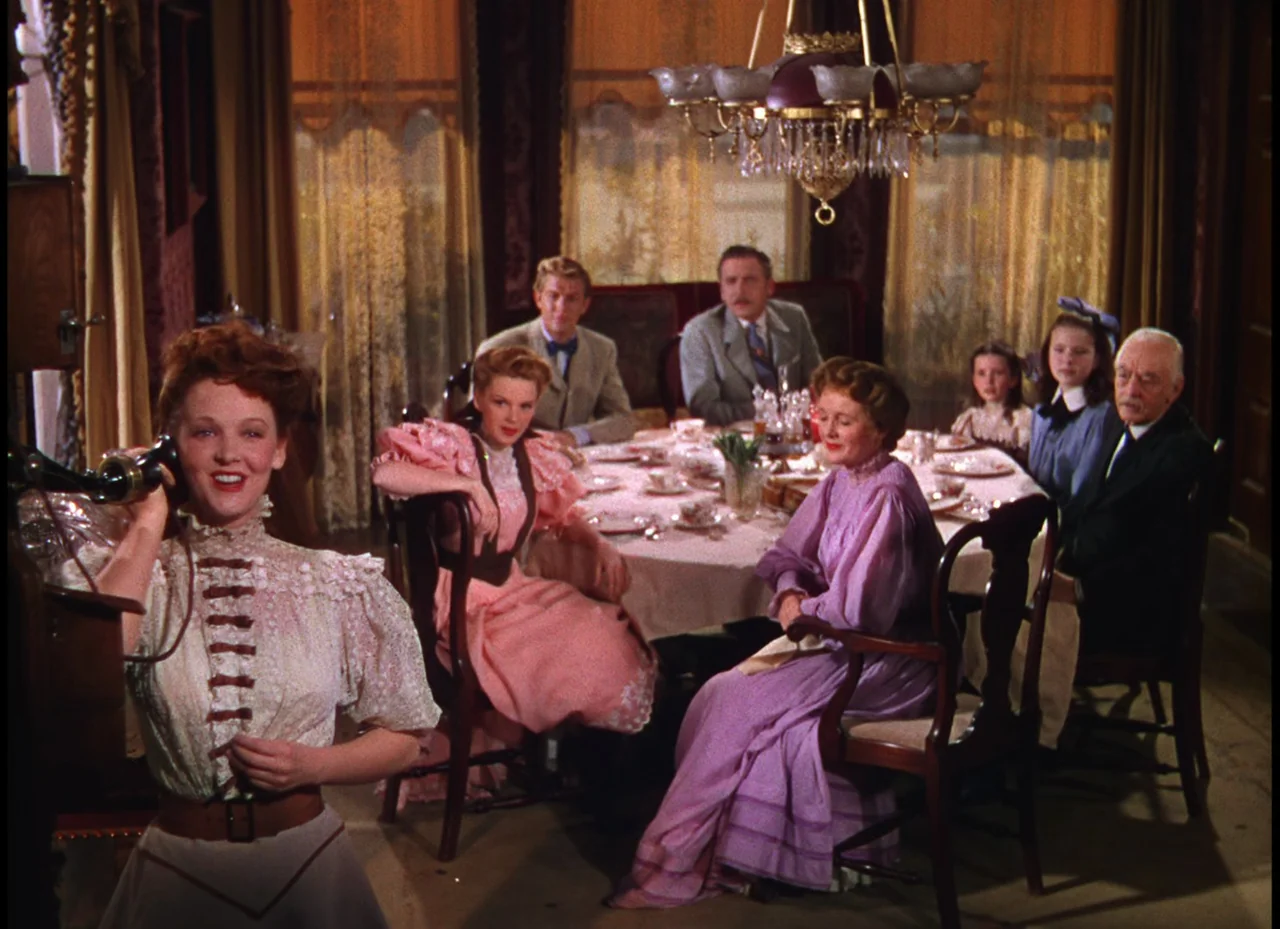 Meet Me In St. Louis (1944) movie still: medium — A formal dining room featuring a large round table surrounded by seated family members. A woman…