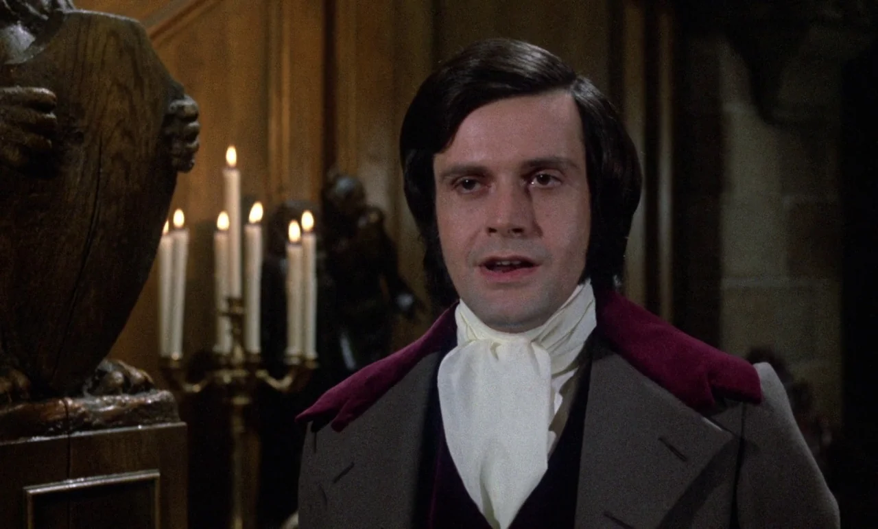 The Horror of Frankenstein (1970) movie still: medium — A dimly lit room with wood-paneled walls and a large ornamental wooden sculpture. A man in…