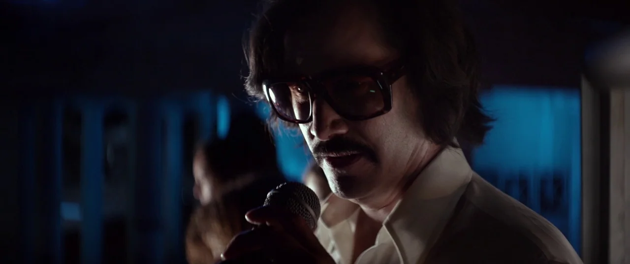 The Bad Batch (2016) movie still: closeup — A dimly lit nightclub interior with deep blue lighting cast on the subject. A man with a mustache and…