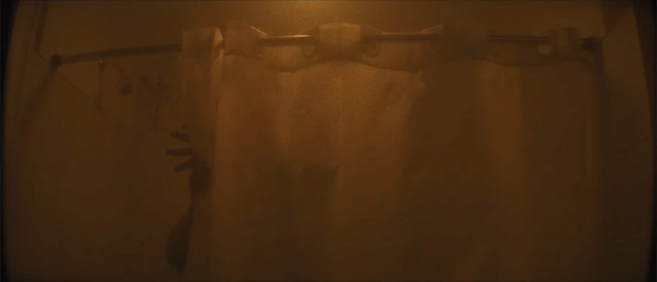 All Fun and Games (2023) movie still: medium — A dark, cramped tiled shower stall is obscured by a translucent plastic curtain. A human hand is…