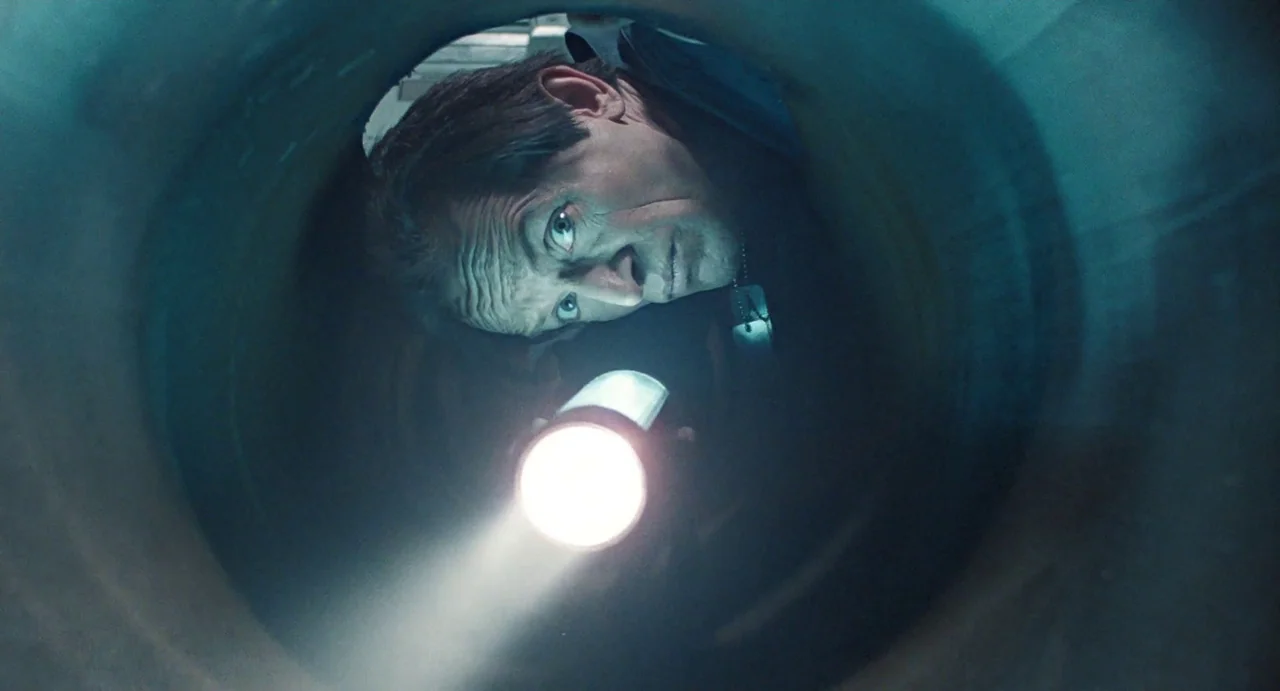 Aliens (1986) movie still: closeup — A dark, cramped, cylindrical metal tunnel curves tightly around a male face. The man holds a bright flashlight…