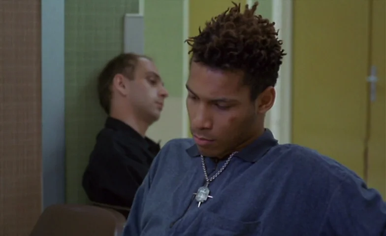 I Can’t Sleep (1994) movie still: medium — A utilitarian waiting area features pale olive wall panels and a vertical door frame. Two men sit near…