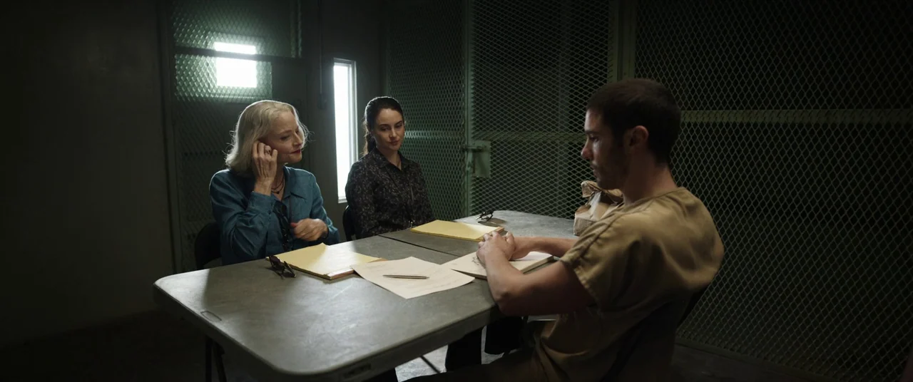 The Mauritanian (2021) movie still: medium — A austere room featuring metallic mesh walls and a grey plastic folding table. Three people sit at the…
