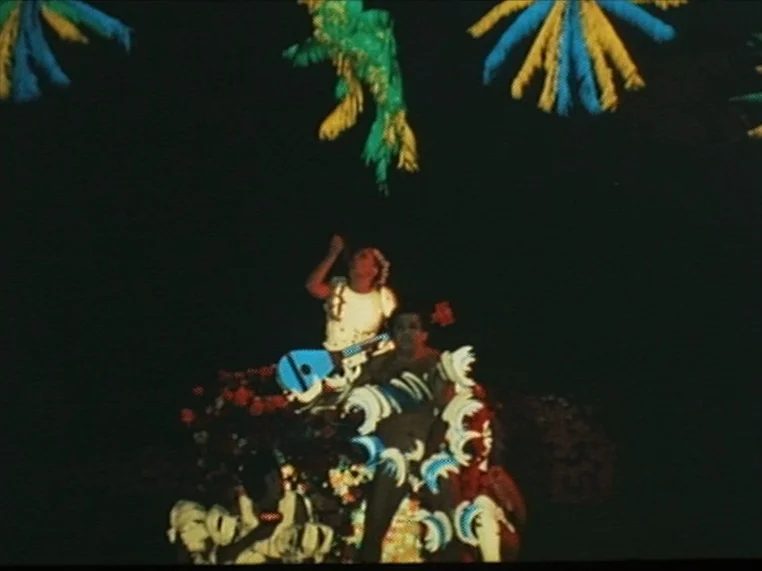 Salome (1972) movie still: wide — A dark night setting features a decorative float covered in colorful, feathery ornaments. Multiple performers…