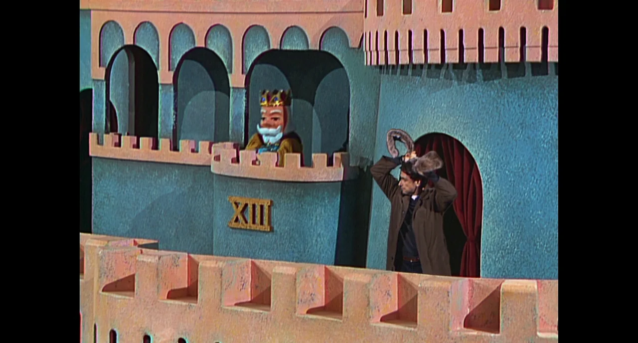 A Beautiful Day In The Neighborhood movie still: wide — A theatrical puppet castle set features pastel blue walls and a small arched opening. A man…