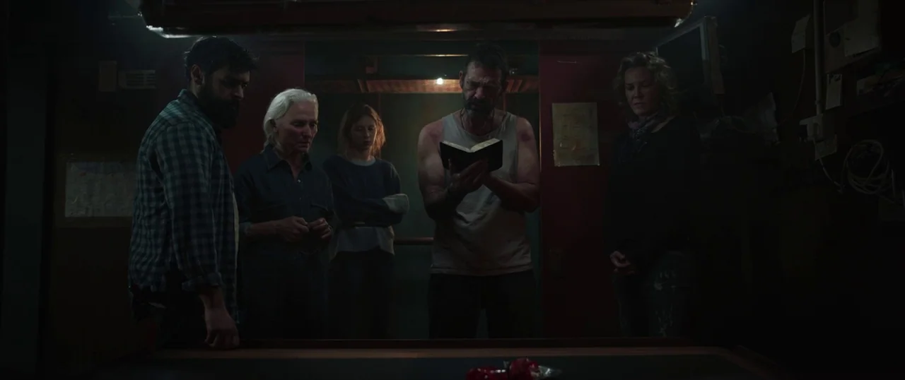 Sea Fever (2019) movie still: medium — A dimly lit, cramped cabin with wood-paneled walls and exposed wires on the bulkhead. Five people stand in a…