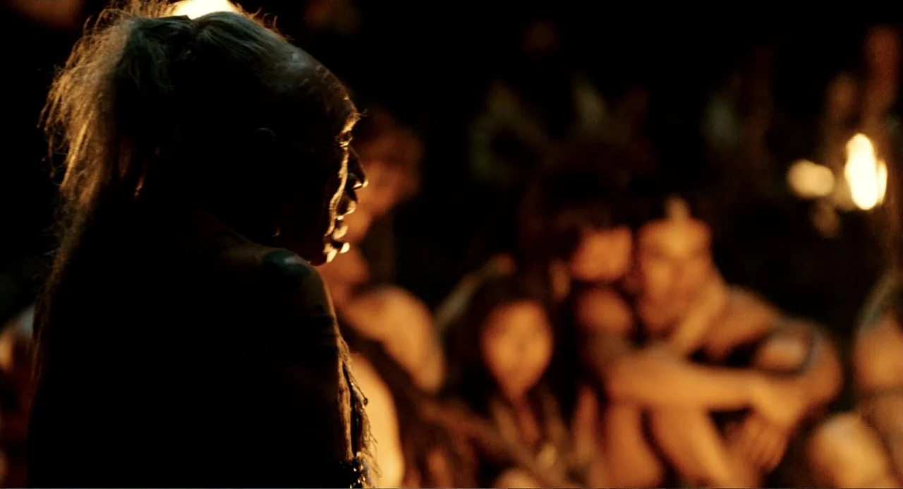 Apocalypto (2006) movie still: medium — A dark night setting in a forest clearing illuminated by a flickering fire. An elderly man with long hair…