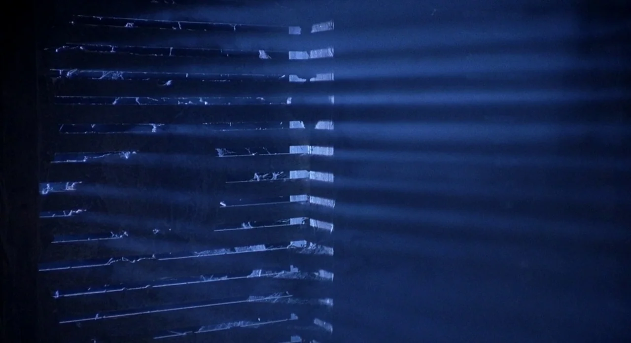 Hellraiser (1987) movie still: establishing — An interior space is shrouded in darkness with light filtering through horizontal window blinds.…