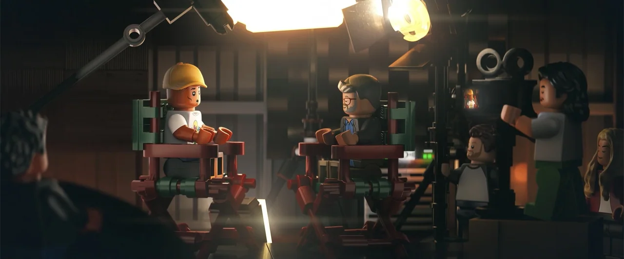 Piece by Piece (2024) movie still: wide — A film studio interior features lego minifigures seated in director chairs on a set. A small crew operates…