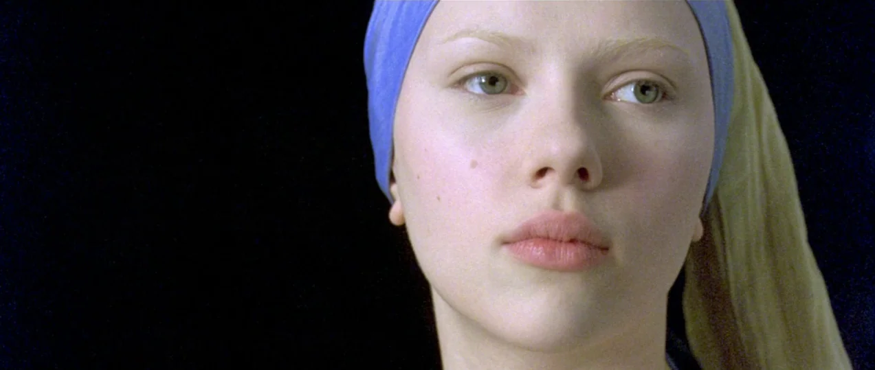 Girl with a Pearl Earring (2003) movie still: closeup — A dark, featureless void serves as the backdrop for a young woman's face. The woman wears a…