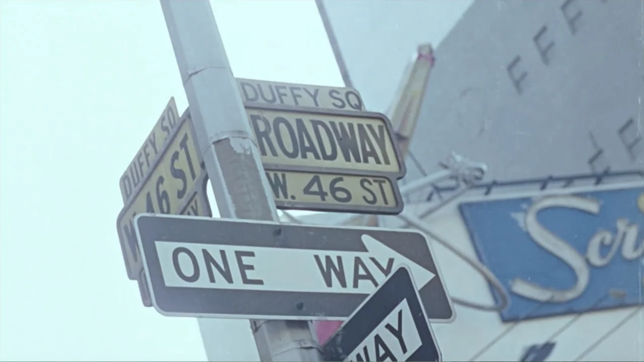 Becoming Led Zeppelin (2025) movie still: closeup — A metal street sign post stands against a bright, hazy sky. Multiple city street signs indicate…
