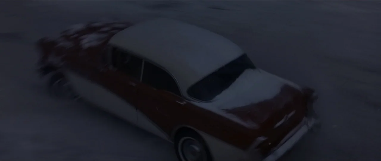 Cobb (1994) movie still: wide — A vintage two-tone automobile travels across a dark, snow-covered surface at night. The vehicle is angled away from…