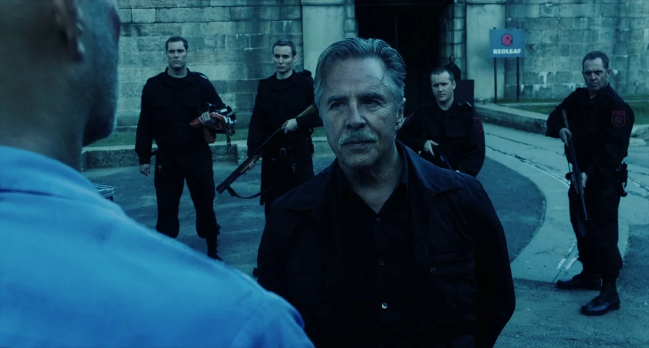 Brawl in Cell Block 99 (2017) movie still: medium — A group of armed men in black uniforms stands before a stone structure. An older man with a…