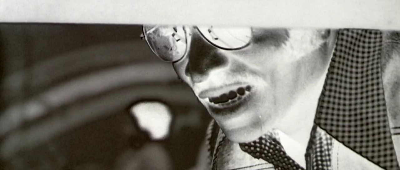 Bones movie still: closeup — A close-up view shows a person in a photographic negative effect. The subject wears glasses and a collared shirt while…