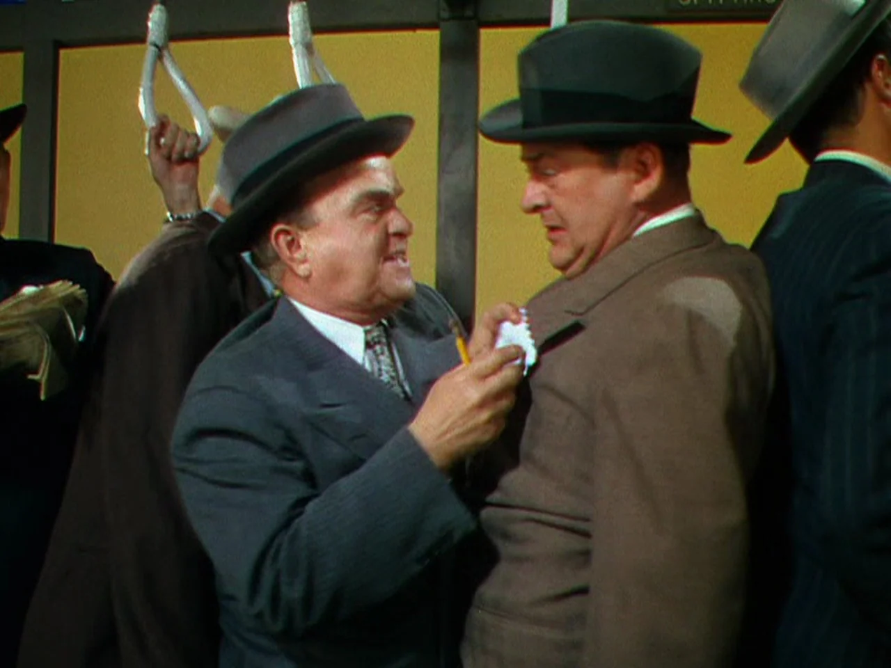 Ziegfeld Follies (1945) movie still: medium — A crowded public transit car with yellow walls and overhead white hand-straps. One man writes on a…