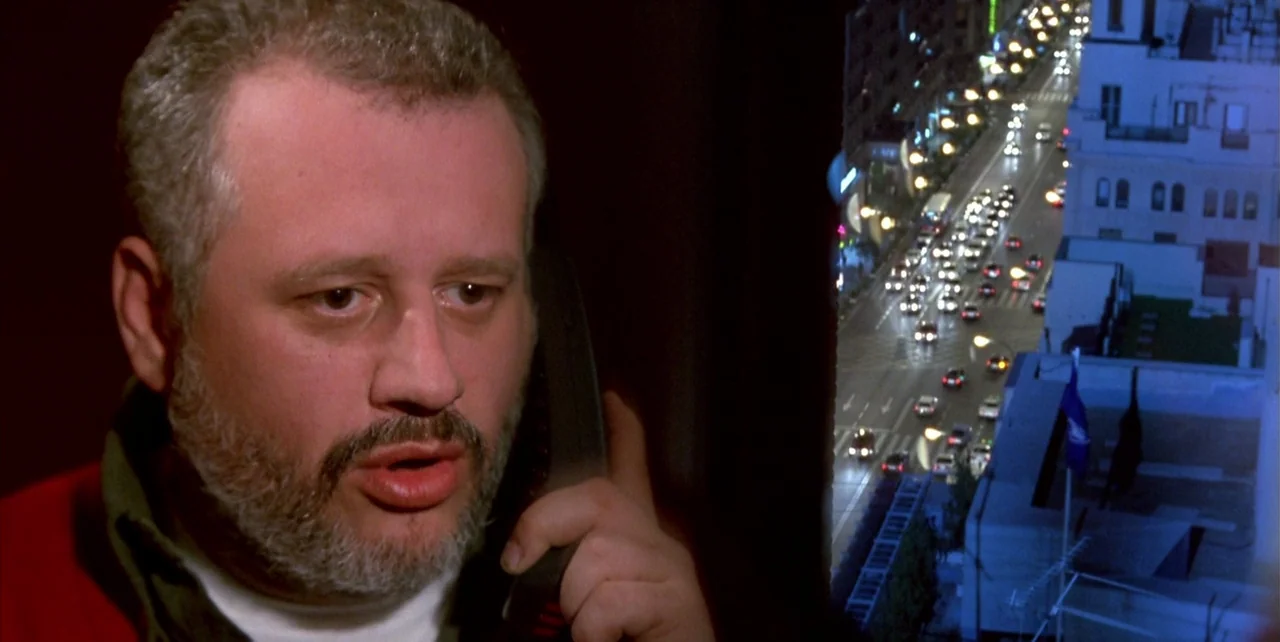 The Flower of My Secret (1995) movie still: closeup — A dark indoor space overlooks a bright city street at night from a high floor. A man with a…
