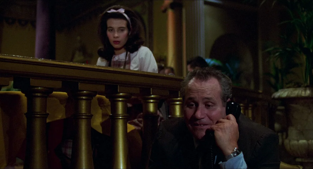 I Wanna Hold Your Hand (1978) movie still: medium — A dimly lit indoor space features ornate golden columns and a decorative balcony railing. A man…