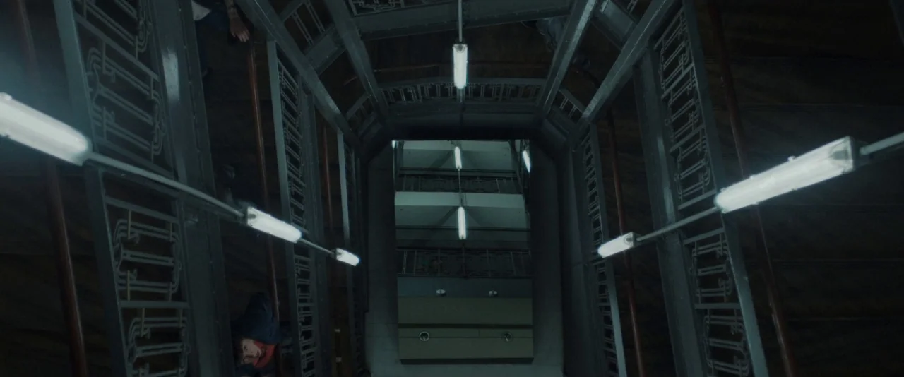 Nocturama (2016) movie still: establishing — A vertical interior stairwell features geometric iron railings and repetitive floor landings. Long…