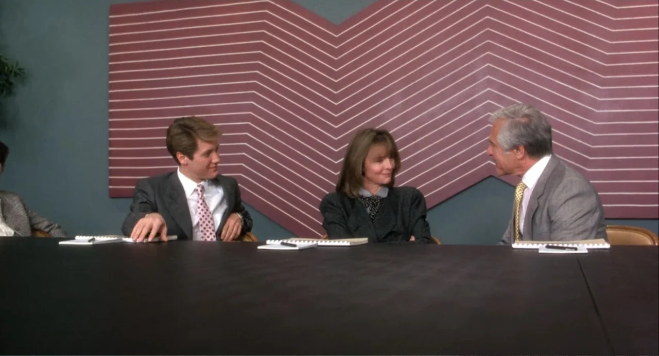 Baby Boom (1987) movie still: medium — A modern office conference room features a geometric chevron pattern on the back wall. Three professionals…