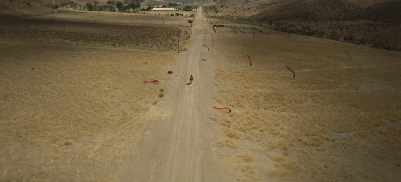 Nope (2022) movie still: wide — A dry, arid desert landscape features a single dirt road cutting through scrubland. A lone rider on horseback…