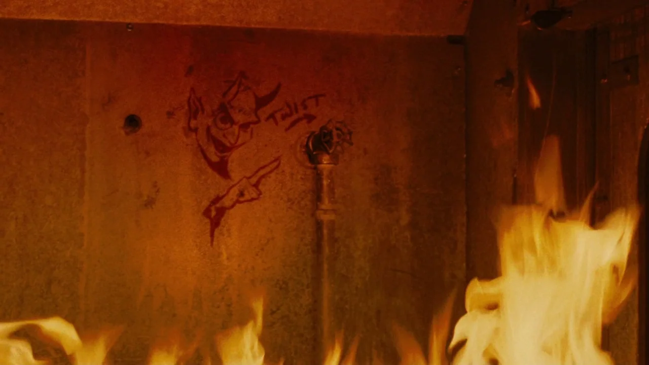 Saw II movie still: closeup — The interior of a metal structure features a crudely drawn devil pointing toward a valve. Flames rise from the bottom…