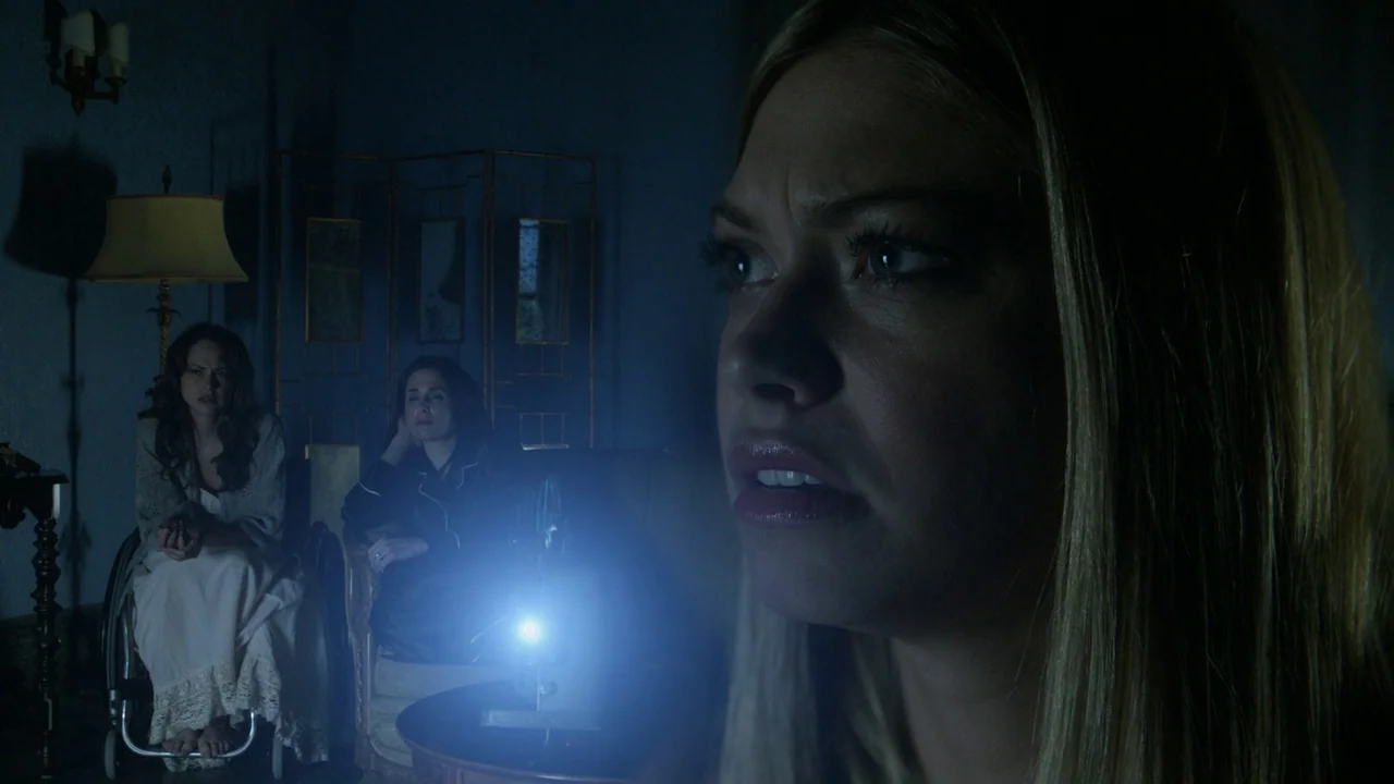 Curse of Chucky (2013) movie still: medium — A dimly lit room features a woman in the foreground watching a bright projection. Two other women are…