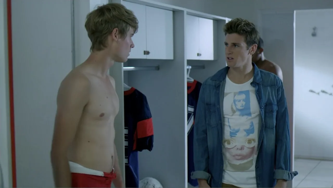 Loco Love (2003) movie still: medium — A brightly lit locker room features white lockers and open shelving with hanging athletic jerseys. Two young…