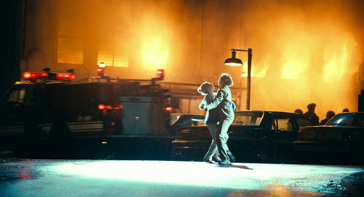 Joker: Folie à Deux (2024) movie still: fullbody — An urban street scene is engulfed in massive flames and thick smoke at night. A young couple…
