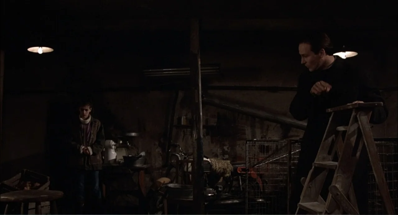 Gorky Park (1983) movie still: fullbody — A dimly lit basement cluttered with wooden items, wire cages, and tools. A man by a ladder observes a…