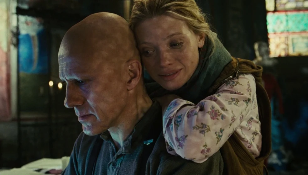 The Zero Theorem (2013) movie still: medium — A dark, textured interior space features stained glass windows visible in the blurred background. A…