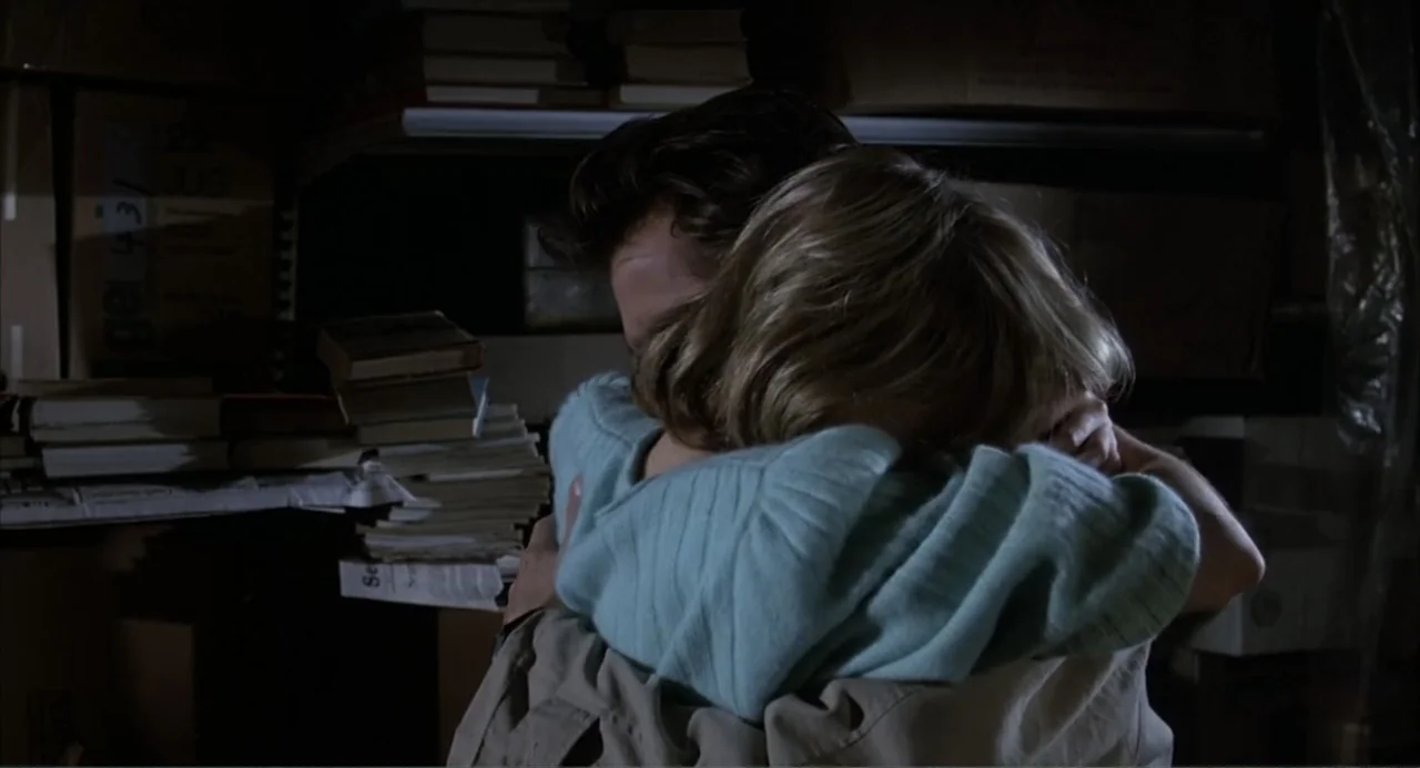 I, Madman (1989) movie still: medium — A dark, cluttered storage room filled with stacked cardboard boxes and paper documents. Two individuals…