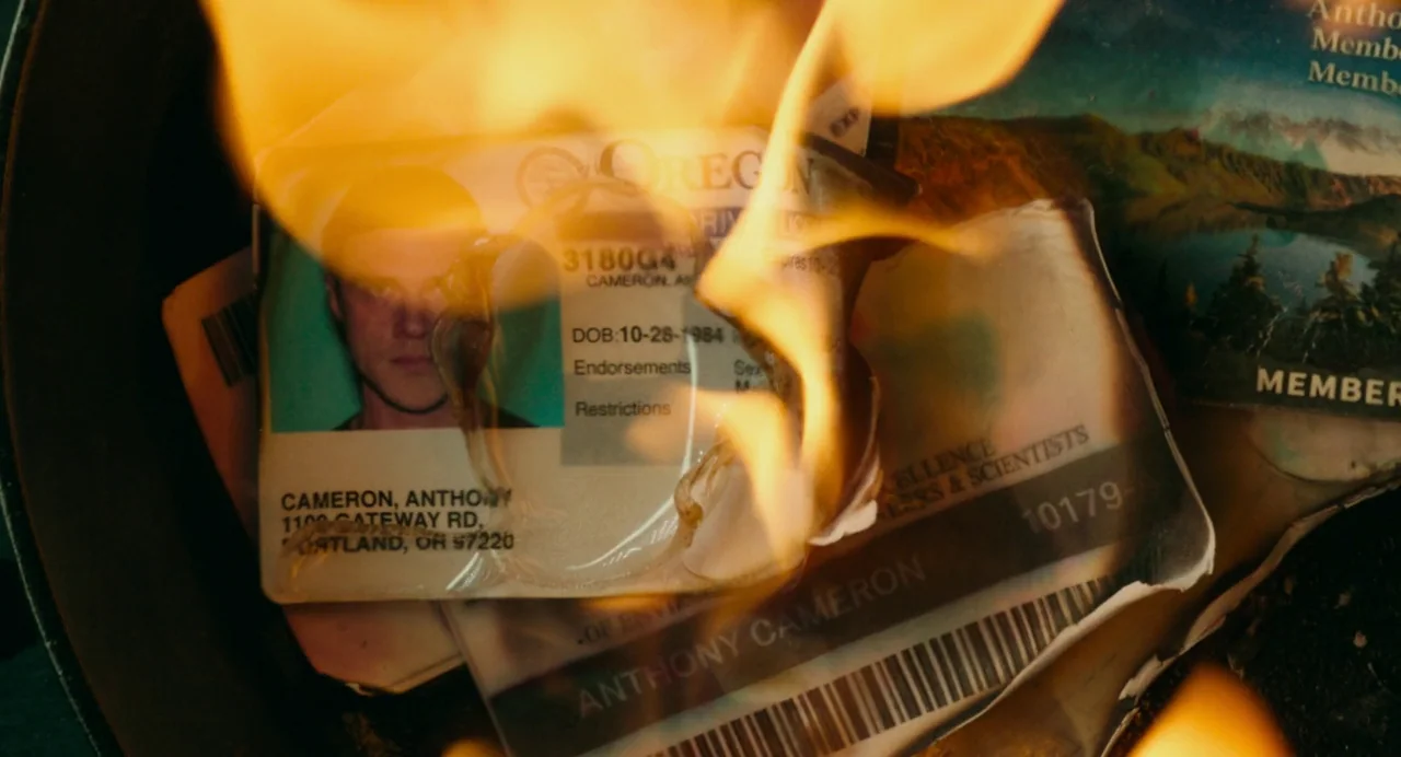 Deep Water (2022) movie still: closeup — Several identification cards and plastic memberships are melting inside a dark metal container. Bright…