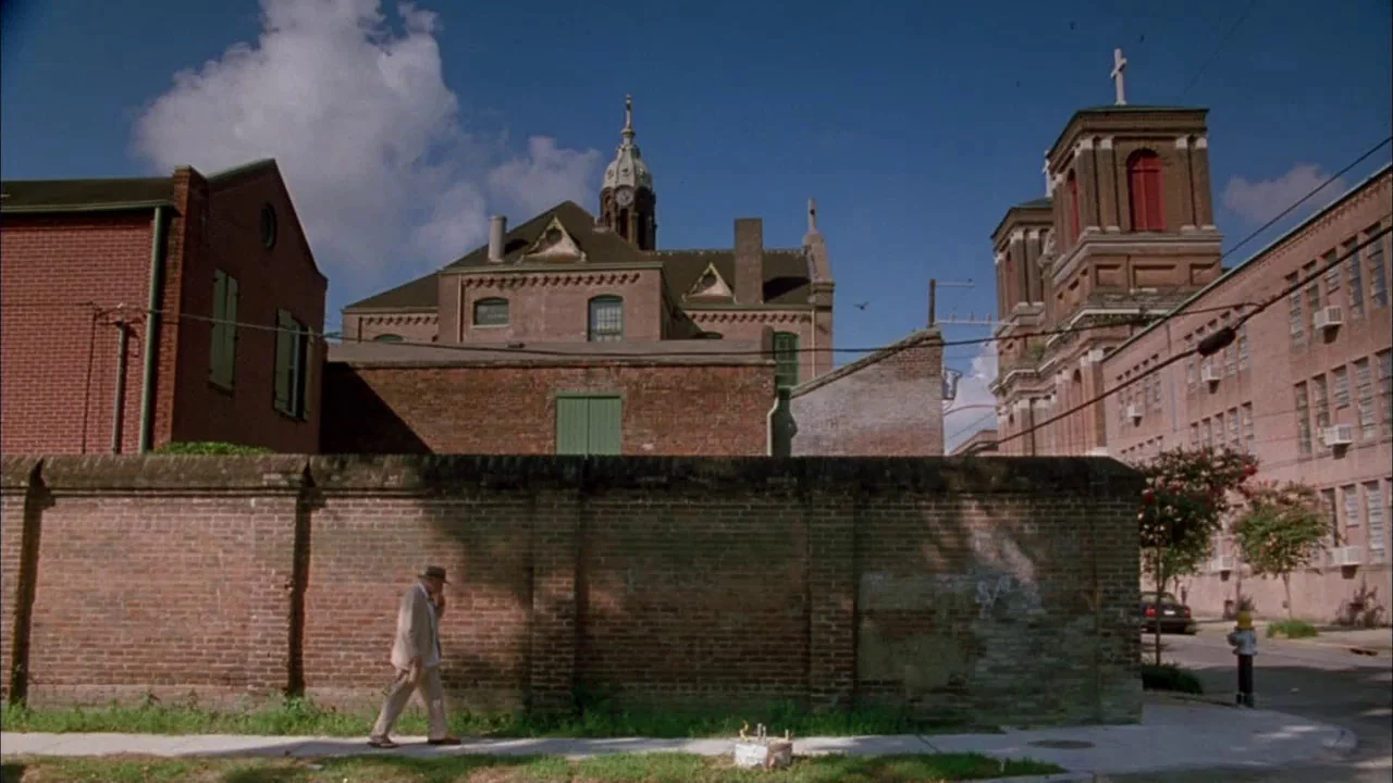 Love Song For Bobby Long (2004) movie still: wide — A man walks along a long brick wall in a neighborhood with historic buildings. Red brick…