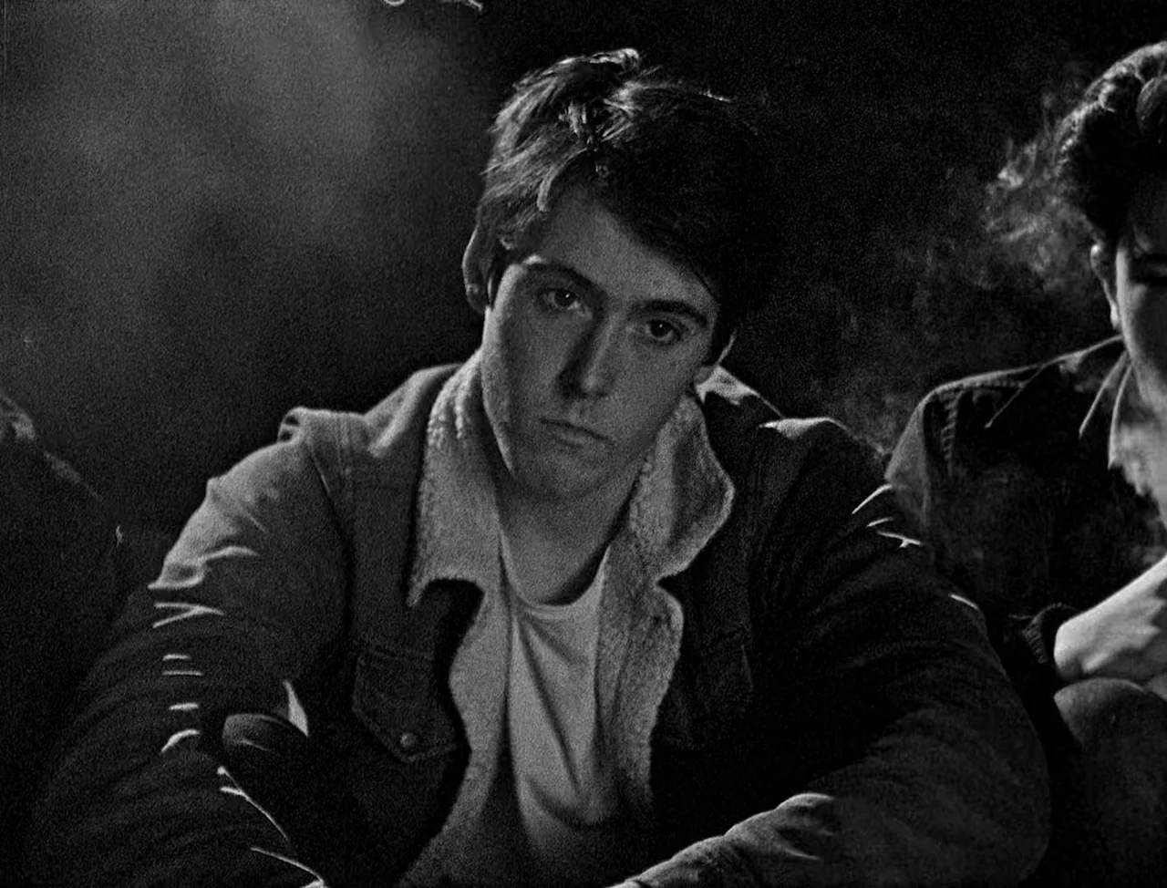 Bait (2019) movie still: medium — A man sits in a dimly lit, dark space with a secondary person visible.