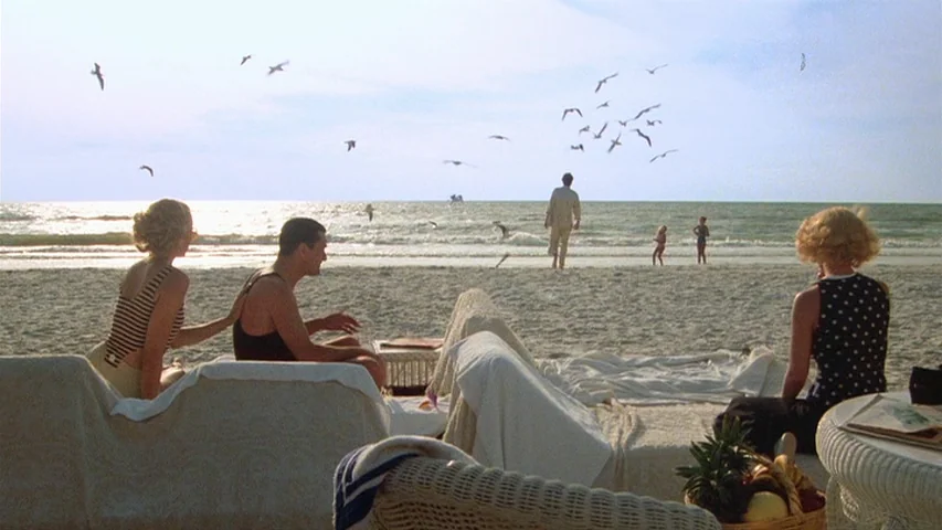 Once Upon A Time In America (1984) movie still: wide — A sandy beach features several people resting on white covered lounge chairs. A man walks…