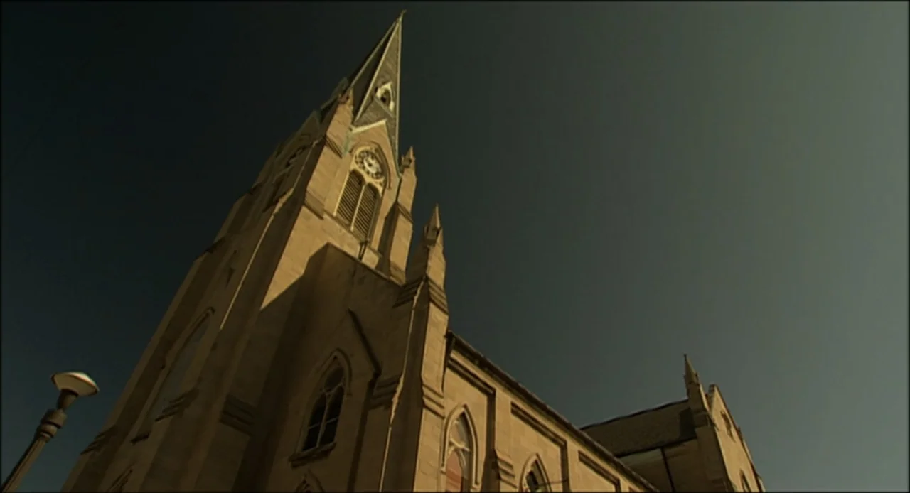 Hard as Nails (2001) movie still: establishing — A stone church building stands against a clear sky during the late afternoon. The structure…