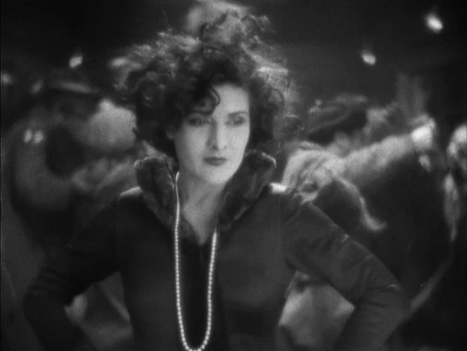 The Last Command (1928) movie still: medium — A dimly lit 1920s dance hall with blurred figures moving in the dark background. A woman in a dress…