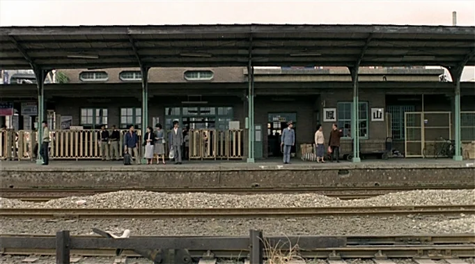 A Time To Love and A Time To Die (1985) movie still: wide — A long, concrete train platform features a covered walkway supported by green metal…