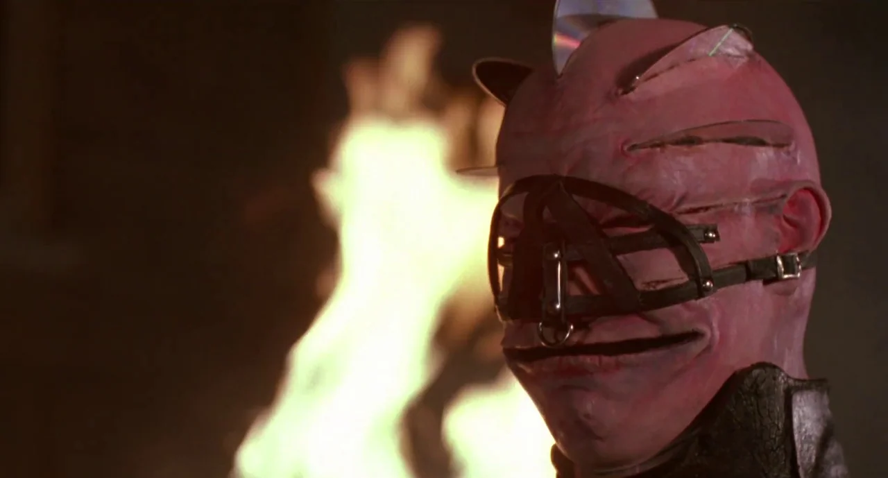 Hellraiser III: Hell on Earth movie still: closeup — A character with a skin-toned mask featuring metallic embedded shards stands outdoors at night.…