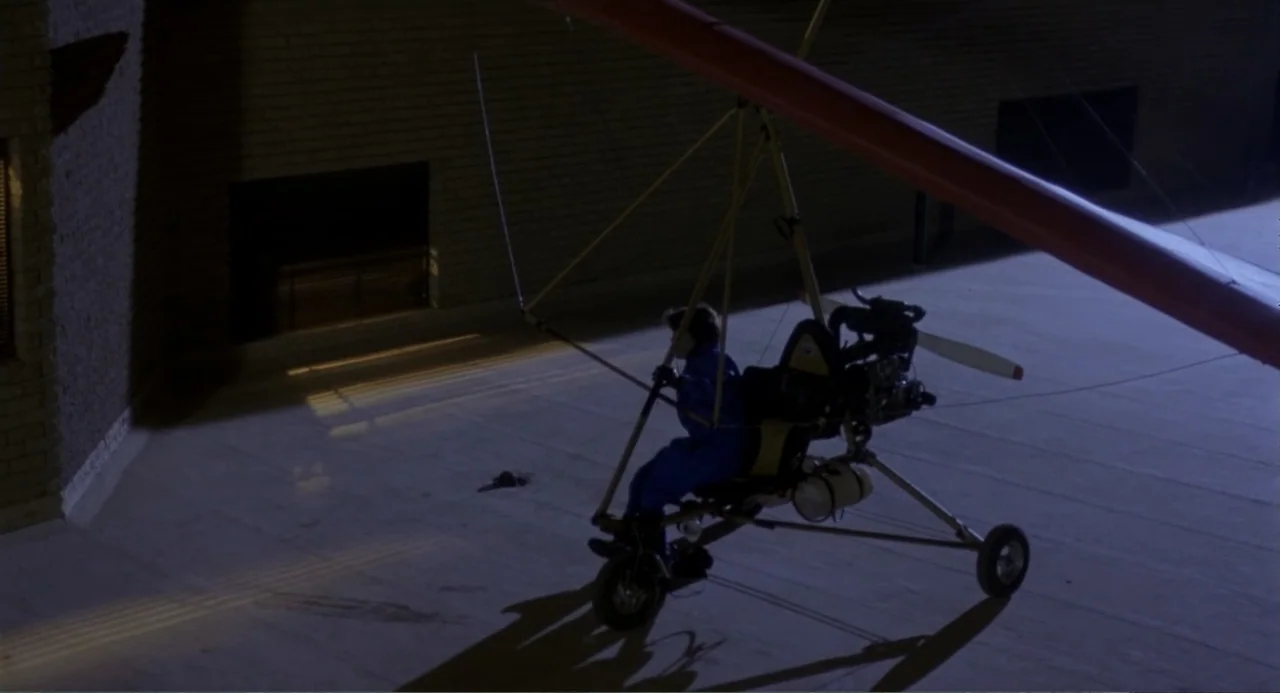 American Ninja 3: Blood Hunt (1989) movie still: wide — A dark, flat industrial rooftop made of concrete at night under artificial light. A person…