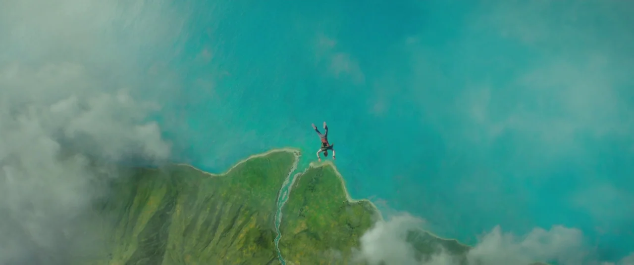 A Wrinkle In Time (2018) movie still: wide — A top-down view shows a rugged green coastline meeting a vast expanse of turquoise water. A lone person…