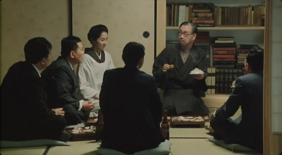 Madadayo (1993) movie still: medium — A traditional Japanese room features tatami floor mats and shelves filled with books. Four men in suits and…