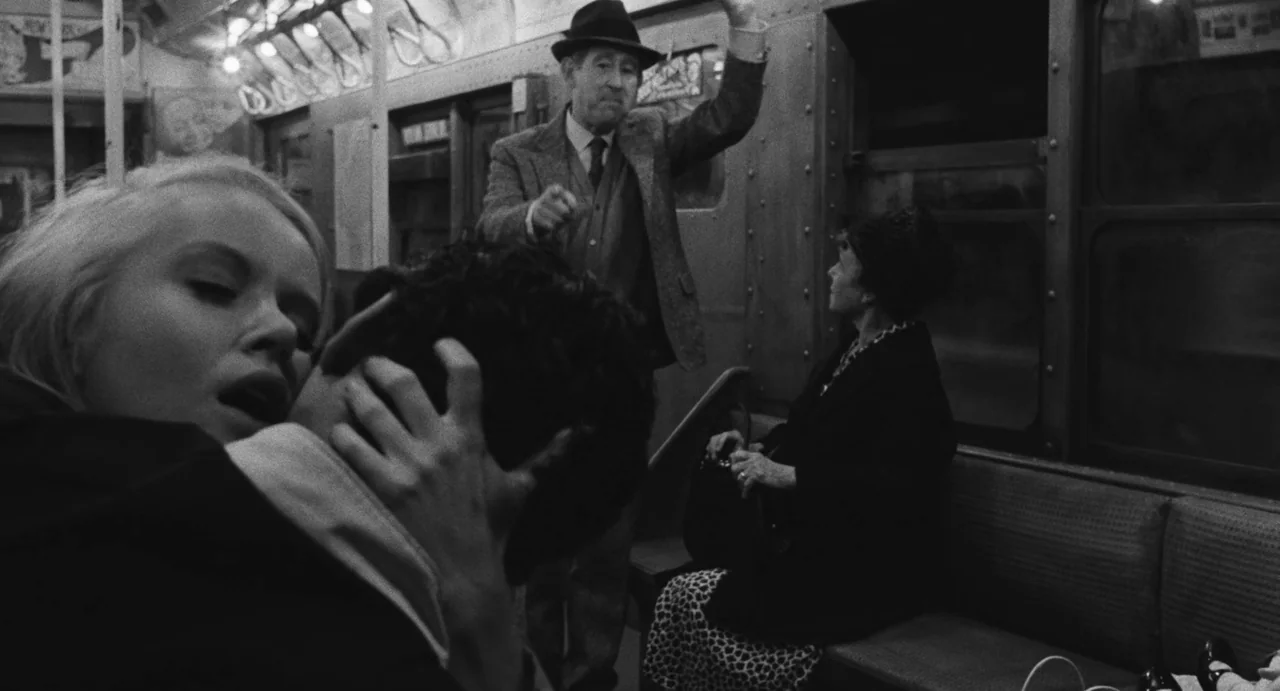 The Incident (1967) movie still: medium — An interior of a vintage subway car with metal seating and overhead lighting panels. A young couple kisses…