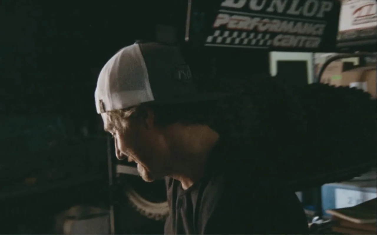 The Greasy Hands Preachers (2014) movie still: closeup — A dark indoor space contains a Dunlop sign and various unidentified mechanical items. A man…