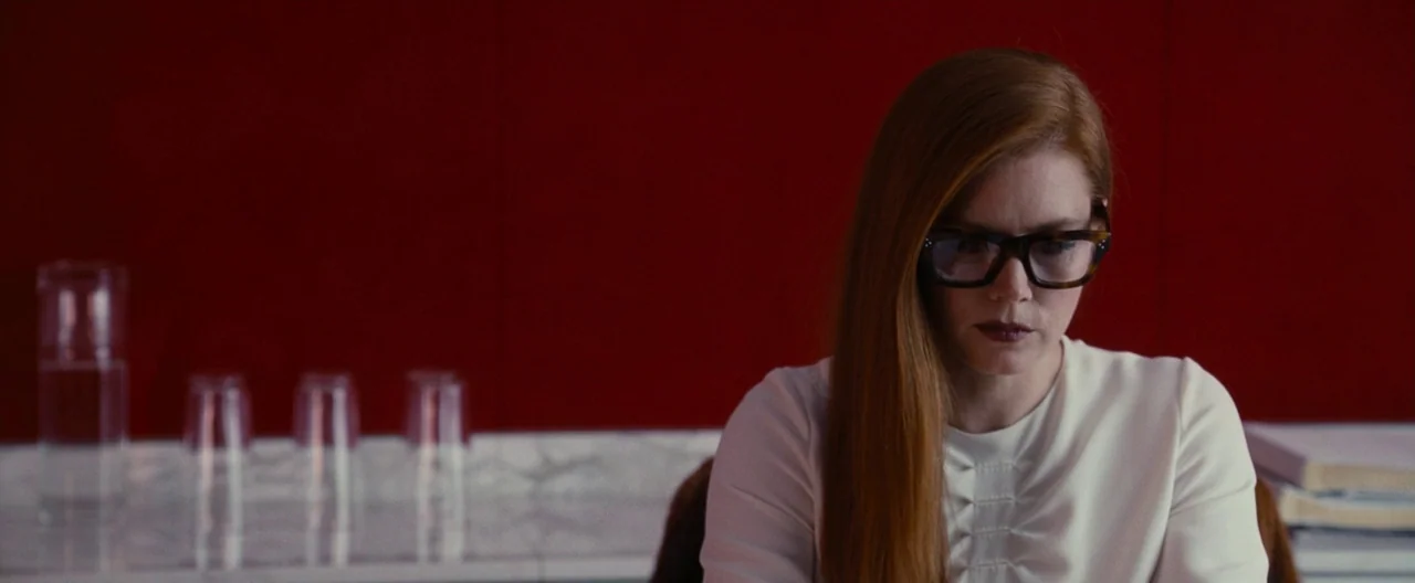 Nocturnal Animals (2016) movie still: medium — A woman sits in front of a flat, monochromatic deep red wall. She looks downward while positioned…